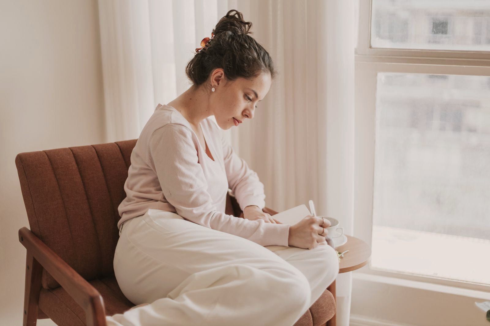 Woman writing in a journal beside a bright window